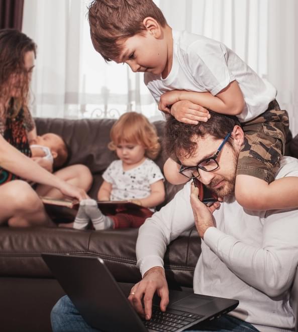 Dad trying to work on laptop while son climbs on his shoulders