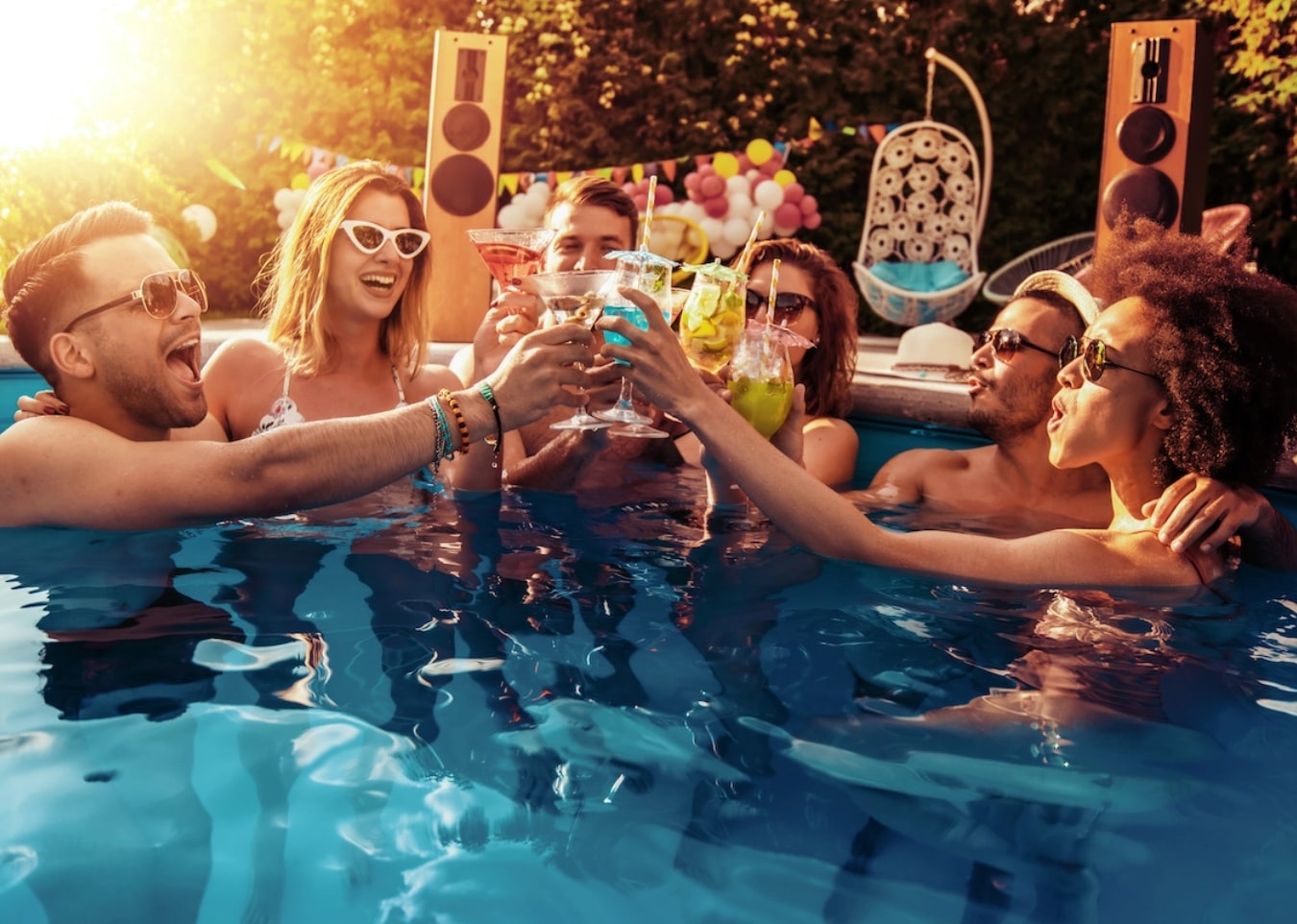 Young people toasting their drinks in a pool at a party